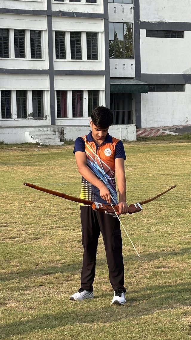 A student setting up an archery shot on the lawn with the bow lowered