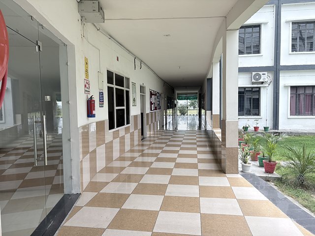 A long checkerboard corridor in the academic block lined with potted plants