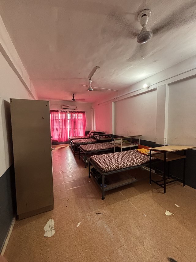 A hostel dormitory wing with made beds and study tables along one side